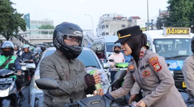 Salah satu Polisi Wanita (Polwan) saat membagikan bunga dan snack kepada pengendara sepada motor